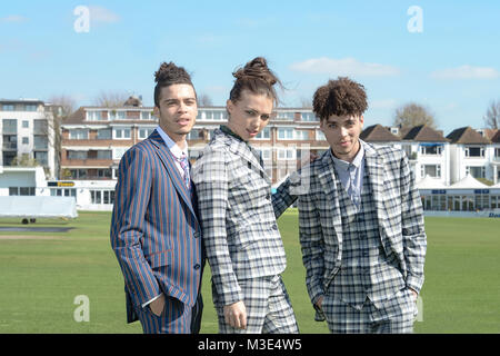 Two well dressed handsome dark skinned guys are at a Cricket Ground . with a beautiful well dressed girl. They wear patterned tailored suits Stock Photo