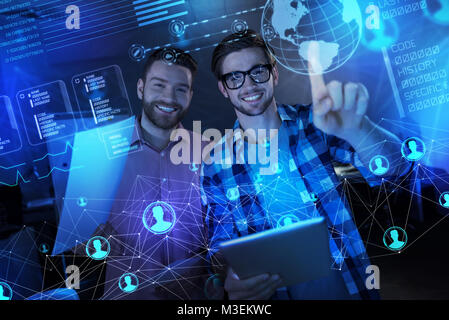 Positive programmers feeling glad while working with transparent screen Stock Photo