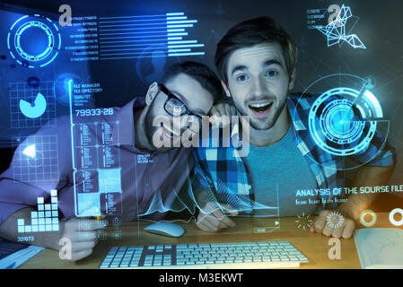 Positive programmers laughing while looking at the modern transparent screen Stock Photo