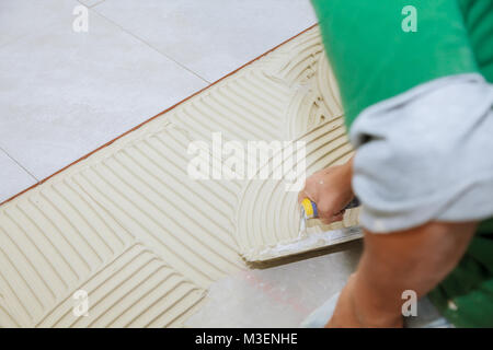 Worker installs tiles on the floor. He put glue using comb trowel. Master puts adhesive Stock Photo