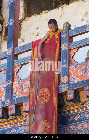 Phobjikha, Bhutan.  Young Monk (Acolyte) Dusting a Floor Carpet, Gangte Monastery (Goemba). Stock Photo