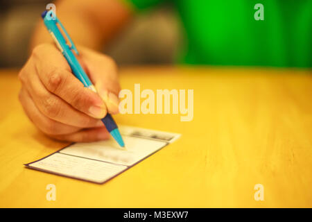 Man's right hand writing on the lucky draw coupon, memo, comment, suggestion or questionnaires on the wooden table in the restaurant or shop concept w Stock Photo