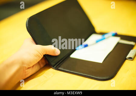 selective focus customer hand receive bill payment receipt in black leather folder holder tray on yellow wooden table background in restaurant, shoppi Stock Photo