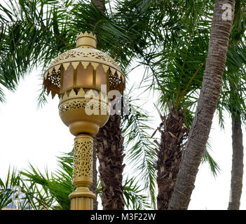 Close up view of ornate vintage golden illuminated lamp post. Palm trees in background. At Disneysea Tokyo. Stock Photo