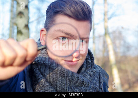 portrait of handsome man looking through a magnifying glass outdoors Stock Photo