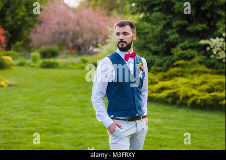 Just married man in casual look with a beard, blue vest, pink velvet tie-bow and peony boutonniere Stock Photo