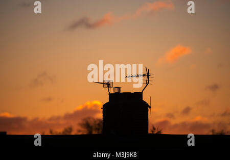 Merton, London, UK. 11 February, 2018. Orange sunrise silhouettes rooftop chimney in Wimbledon. Credit: Malcolm Park/Alamy Live News.