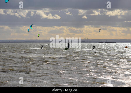 Kite surfers took to the Thames Estuary off Thorpe Bay, Southend on Sea, in strong but chill winds with the industrial Isle of Grain in Kent and a section of D-Day Mulberry Harbour as a backdrop Stock Photo