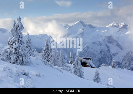 Idyllic old wooden alpine chalets covered with snow with a beautiful mountain landscape in the background, Velika planina, Slovenia. Stock Photo