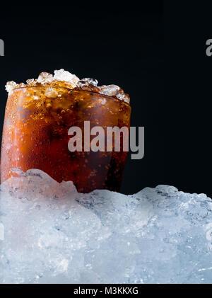 Soft drink with crushed ice cubes in glass put on pile of ice cubes on dark background with copy space. There is a drop of water on the transparent gl Stock Photo