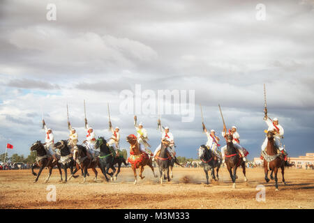 Horses and riders charging with the horses and shooting muskets reenacting war attack scenes Tbourida in Mzoudia Morocco Stock Photo