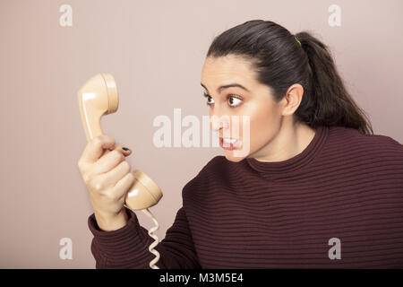 Angry irate woman gnashing her teeth and snarling at the telephone receiver she is holding in her hand Stock Photo