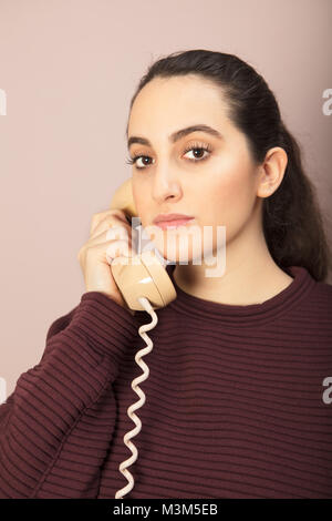 Attractive woman listening to a telephone conversation on a terrestrial line looking thoughtfully at the camera with a serious expression Stock Photo