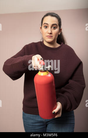 Young woman pointing a red fire extinguisher forwards towards the camera with a serious expression and focus to the canister Stock Photo