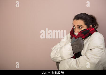 Cold woman snuggling down into her warm scarf and thick winter jacket knitted cap as she hugs herself to keep warm Stock Photo