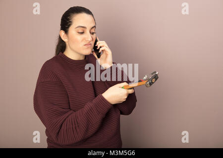 Helpless woman holding hammer with monkey wrench while talking on phone hands in a DIY concept Stock Photo