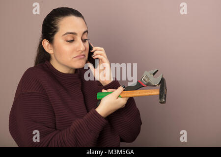 Irritated woman holding hammer with wrench talking on phonehands in a DIY concept Stock Photo