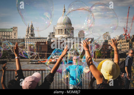 London (UK) - August 2017. Young kids having fun with soap bubbles made by a street performer on the South Bank. Stock Photo