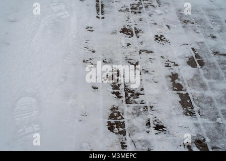 In winter, a snow-covered paving block in the city. Footprints from boots in the snow. Sidewalk in the winter in the snow. Stock Photo