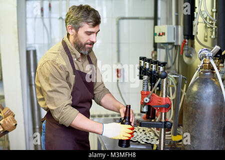 Content handsome technician putting beer in bottles at factory Stock Photo