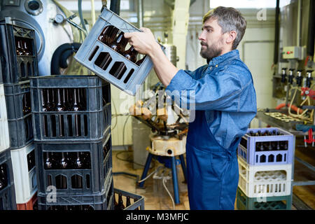 Serious bearded mover in uniform stacking boxes with beer bottle Stock Photo