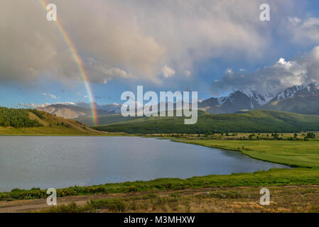 Scenic view with a rainbow after the rain above the mountains, lake and forest against a blue sky with clouds in the summer Stock Photo