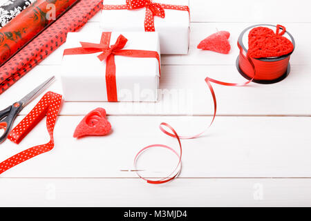 Gift boxes wrapped in white paper and red ribbons, hearts, candles, and a working surface for festive gift packing for Valentine's Day, Christmas, New Year or Birthday. Stock Photo