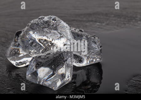 Four ice cubes on black slate board with drops of water Stock Photo