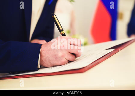 The pen in the right hand signs papers with a shallow depth of field Stock Photo