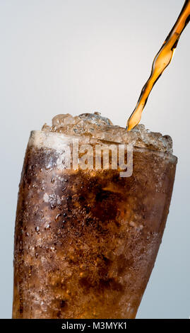 Closeup of soft drink pouring to glass with crushed ice cubes isolated on white background with copy space. There is a drop of water on the transparen Stock Photo