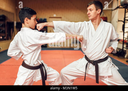 Martial arts karate masters in white kimono and black belts, self-defence practice in gym Stock Photo