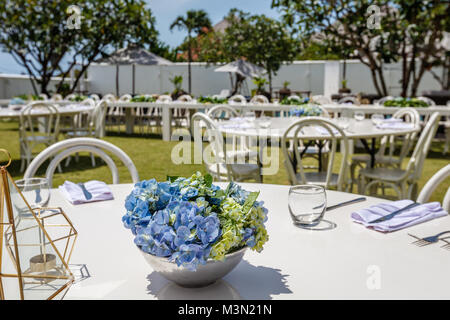 Dinner set up with Hortensia flowers for a wedding. White wooden tables and chairs. Stock Photo