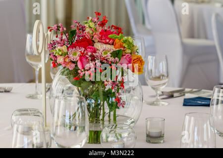 Glass round vase with bright bouquet of flowers on a table set up for dinner. Stock Photo