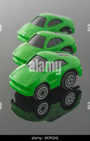 Three green toy cars on reflective background. Metaphor Green cars, Tesla vehicles, carbon footprint, Car Tax, electric vehicles, AOC Green New Deal Stock Photo