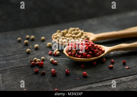 Close up studio shot of pink and white peppercorn in wooden spoons on dark background Stock Photo