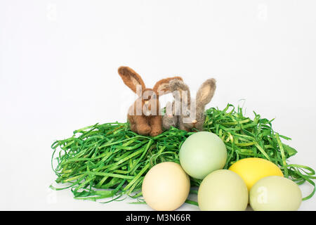Group of Three Small Felted Bunny Rabbits on Green Grass with Colored Eggs Stock Photo