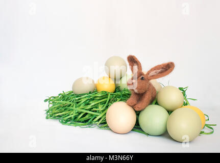 Felted Brown Small Bunny Rabbit with Green Grass and Colored Eggs on White Background Stock Photo