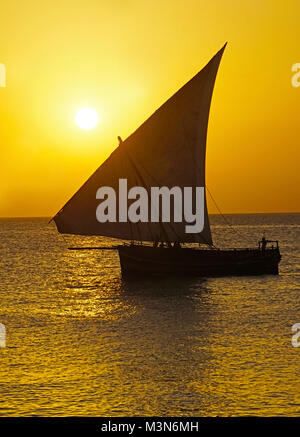 Traditional dhow sailing at sunset off shore of Stone Town In Zanzibar. Stock Photo