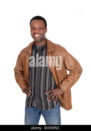 A handsome young African American man standing smiling in a brown leather jacket with his hands on his hips, isolated for white background Stock Photo