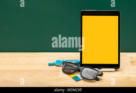 Blank yellow screen tablet with eyeglasses,pencil on wood table top with green blackboard,Education concept.e-learning.clipping path screen Stock Photo