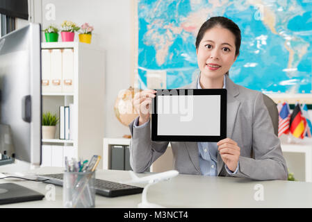 confident attractive female travel agent company office worker holding mobile pad computer looking at camera and showing white blank empty screen. Stock Photo