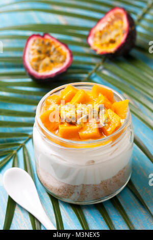 cheesecake in a jar  with tropical fruits: mango, passionfruit.  kiwi slices, orange and passionfruit on straw background Stock Photo