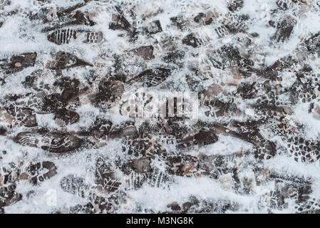 Footprints of boots on the snow in city on the nature. Winter pattern on the asphalt, traces of pedestrians. Stock Photo