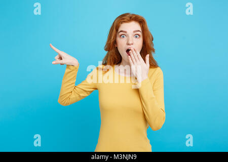 Close up Portrait young beautiful attractive redhair girl with shocking with something and pointing finger. Blue Pastel Background. Copy space. Stock Photo