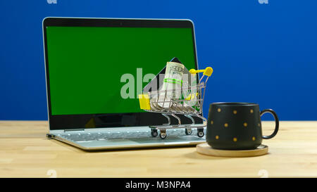 E-commerce retail shopping concept with miniature shopping cart and modern laptop against chroma key background. Stock Photo