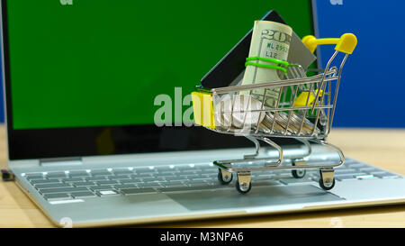 E-commerce retail shopping concept with miniature shopping cart and modern laptop against chroma key background. Stock Photo