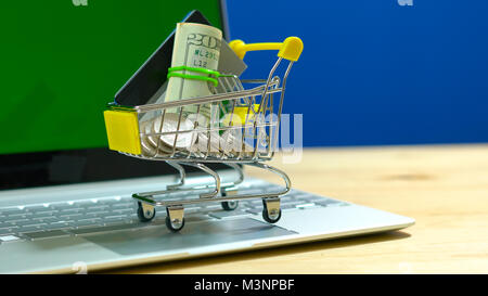 E-commerce retail shopping concept with miniature shopping cart and modern laptop against chroma key background. Stock Photo