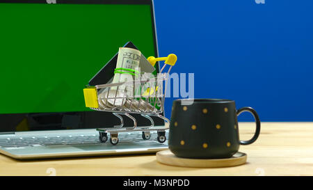 E-commerce retail shopping concept with miniature shopping cart and modern laptop against chroma key background. Stock Photo
