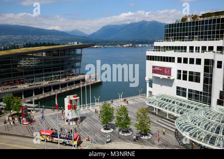 Panorama Vancouver BC waterfront Canada Place harbor, tourists ticket kiosk tour bus people shopping restaurants blue sky green mountains background Stock Photo