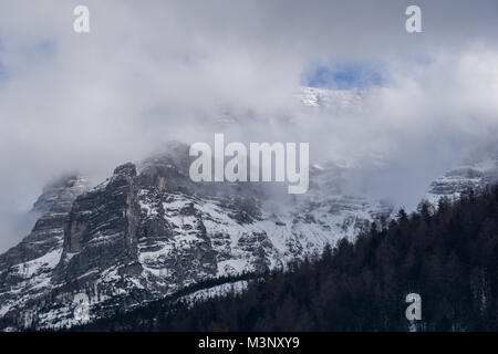 A small window in the clouds shows the mountain top covered in snow and some blue sky Stock Photo